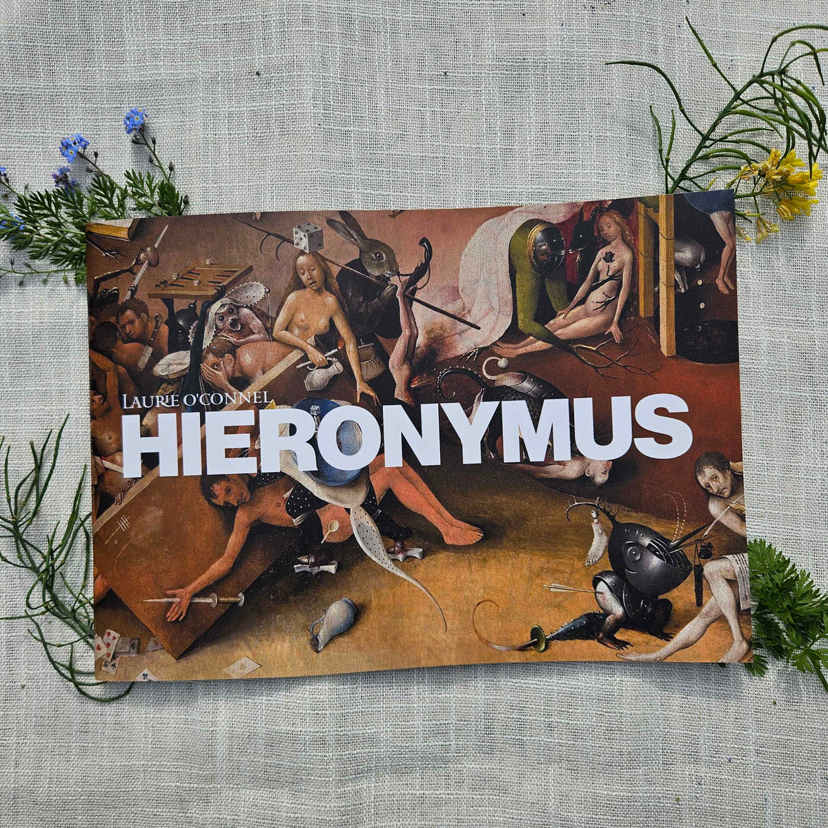 Book titled 'Hieronymus' by Laurence O'Connor on a cloth surface surrounded by plants.