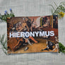 Book titled 'Hieronymus' by Laurence O'Connor on a cloth surface surrounded by plants.